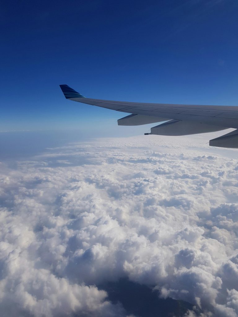 View of airplane wing above fluffy clouds under clear blue sky, perfect for travel and aviation themes.